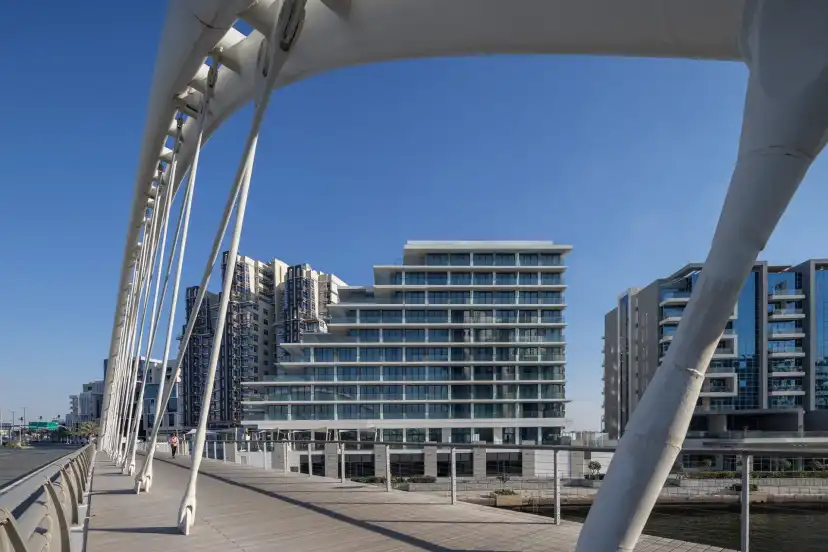 Footbridge arch at Al Raha Beach with a white banded residential building in the distance